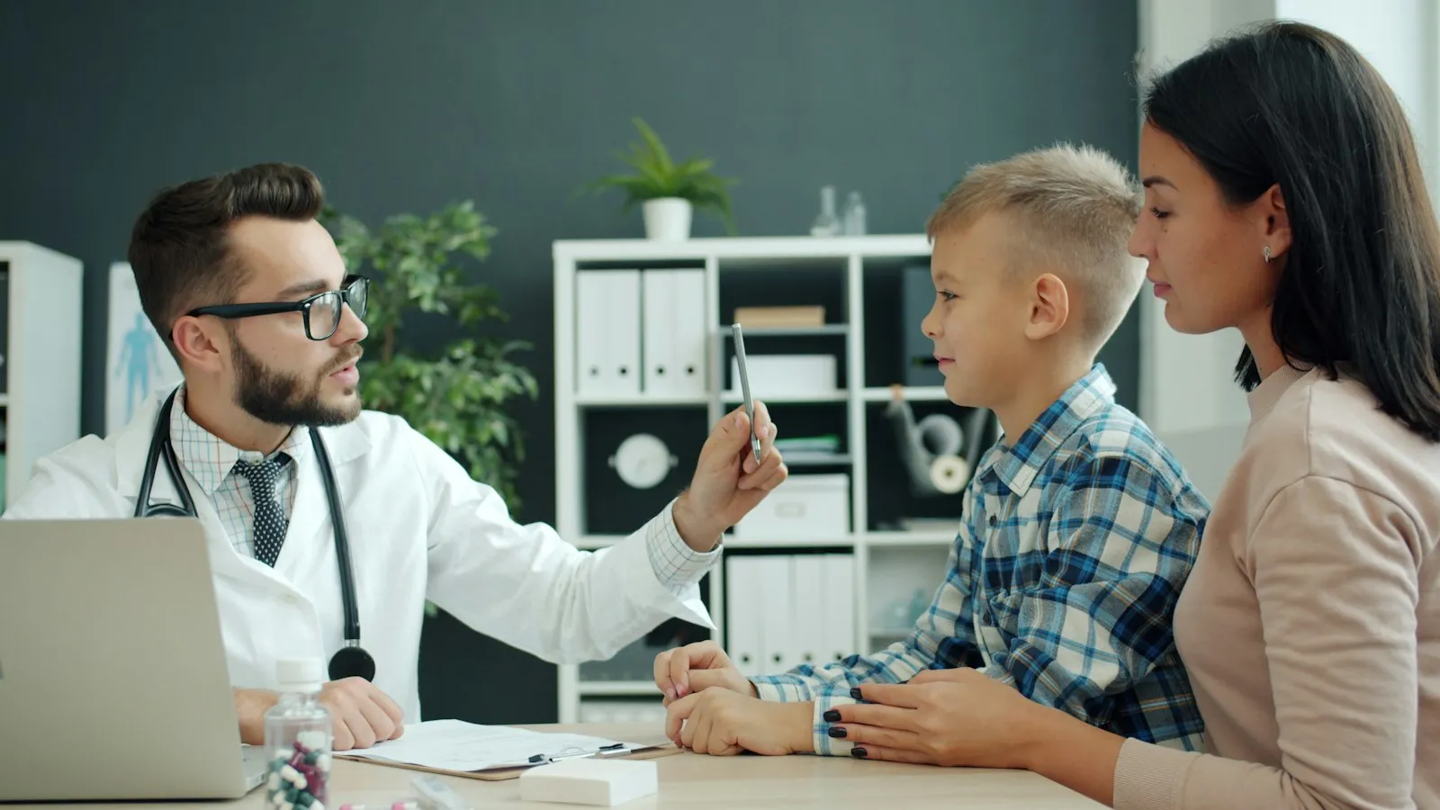 Doctor examining a young boy with his mother in the exam room