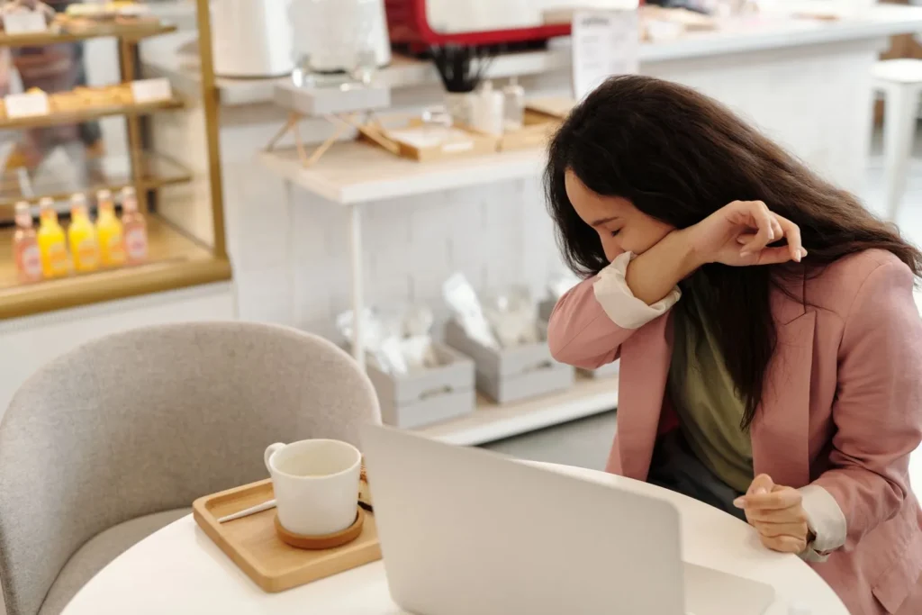 Woman coughing into her elbow at a table