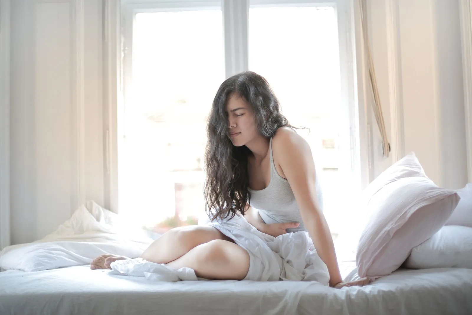 Woman sitting on her bed holding her lower stomach in pain