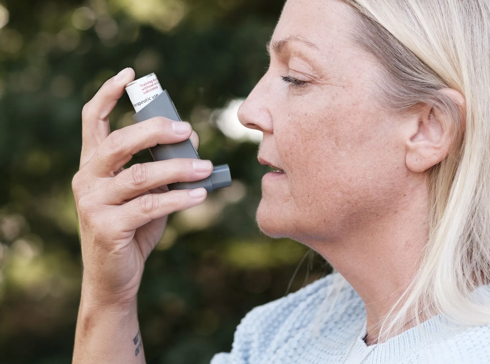 Woman using an asthma inhaler outdoors